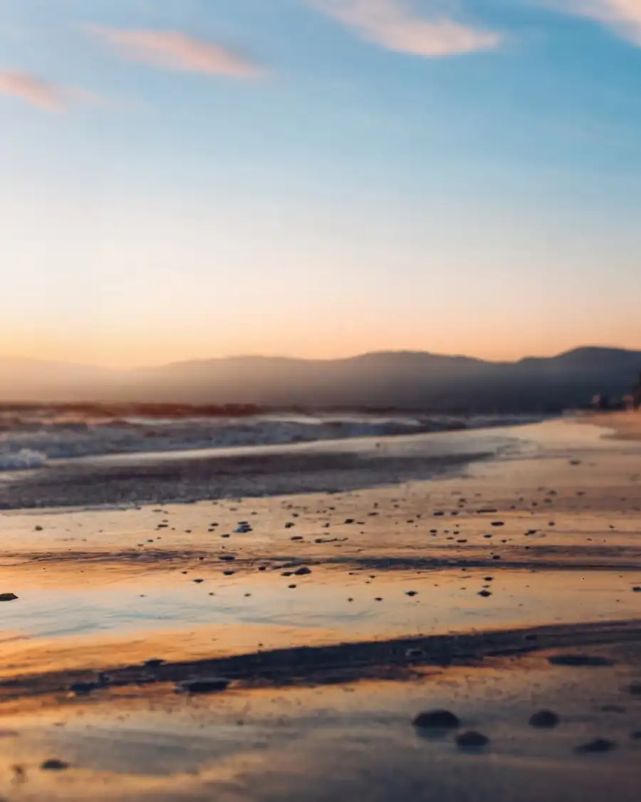 Editing Beach With A Body Of Water And Mountains In The  Background